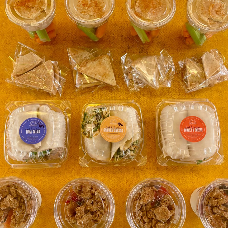 Overhead display of packaged salads, wraps, vegetable snack cups, and bowls arranged on a wooden table.
