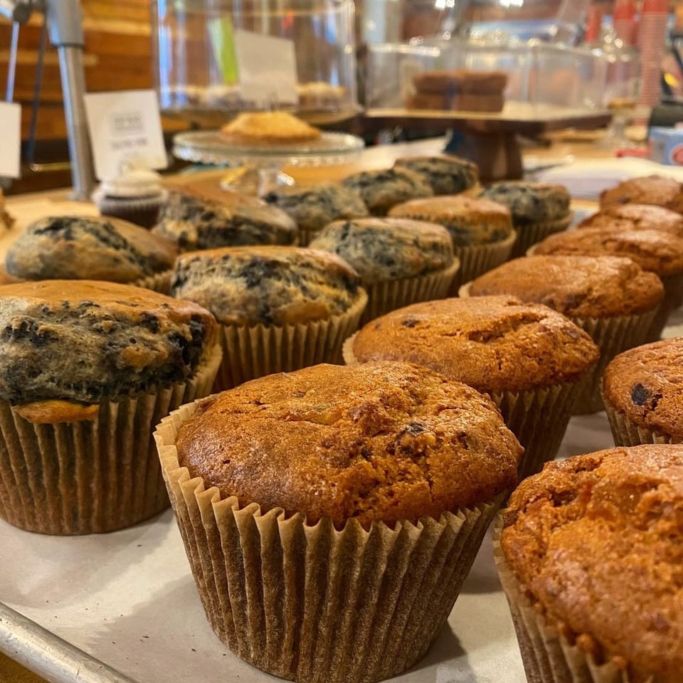 Rows of golden and blueberry muffins in paper liners displayed on a bakery counter.