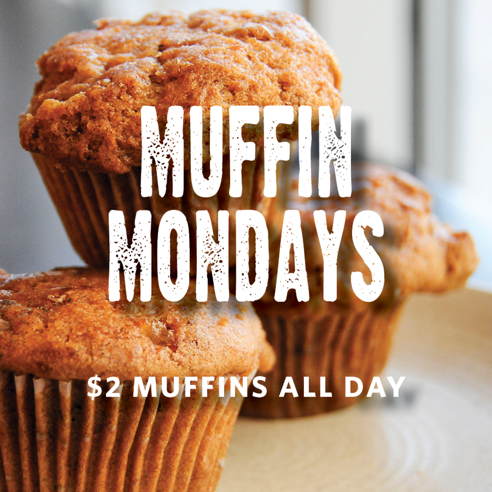 Three golden-brown muffins on a table with promotional text reading “Muffin Mondays” and “$2 muffins all day.”
