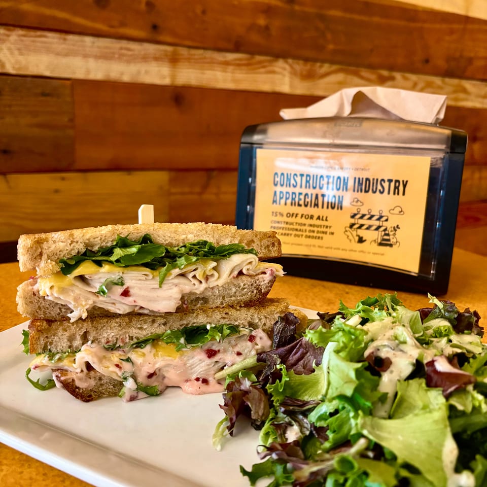 Turkey and cheese sandwiches with leafy greens and creamy dressing served on a white platter against a warm wooden wall.
