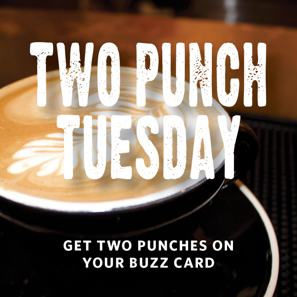 Close-up of a latte in a black cup with foam art, overlaid text promoting two punches on a buzz card.